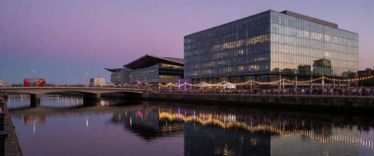 A twilight waterfront cityscape with a glass media building, a bridge crossed by a red double-decker bus, reflections in the water